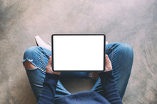 Top View Mockup Image Of A Woman Holding Black Tablet Pc With Blank White Screen While Sitting On The Floor