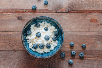 Wall Mural - cottage cheese in a bowl with blueberries and honey for breakfast on wooden background. top view