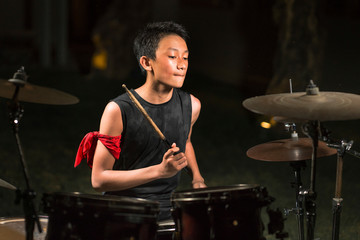 Asian American mixed teenager playing drums at home garden . cool and handsome young boy practicing on drum kit rehearsing passionate in badass rock band look