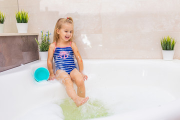 little smiling blonde girl in blue swimsuit splashing in a big modern bathroom with foam. .kids hygi