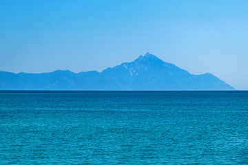 Mount Athos in Greece on a sunny day in summer against a blue sky. Beautiful silhouette of Mount Athos in Greece in the Aegean Sea. Calm seawater surface.