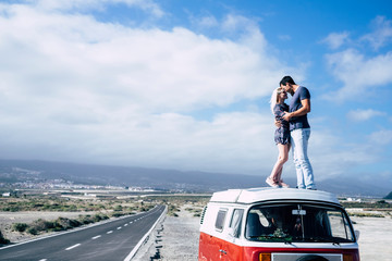 Young couple in love enjoying the travel on a vintage van standing on the roof and hugging with kiss - youth people in outdoor leisure activity and transport