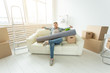 © satura_ - Positive young man sitting on the sofa with his things in the new living room after the move. Concept of housing affordability for young people.