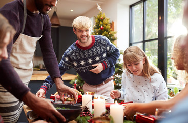 Group Of Friends Sitting Around Dining Table At Home As Christmas Dinner Is Served