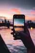 View through a smart phone screen with blurry background of a city at colorful sunset light. A girl holding a phone and taking photos of a urban scene at night. Frankfurt am Main in Germany