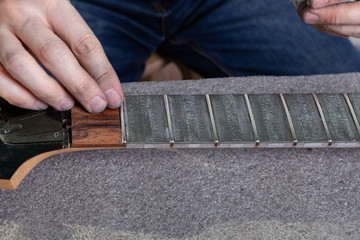 the master removes masking tape with paste from the guitar neck after polishing frets.