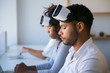 © Mangostar - Team of VR developers working on project. Man and women wearing VR headset, sitting at long desk, using laptops and tablets. Virtual reality concept