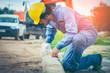 © brain2hands - Asian civil engineer with Beard He wears the blue uniform worker and wears a yellow safety helmet. Using a plane measuring the pavement for road construction.