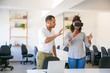 © Mangostar - Young woman in VR glasses standing in office, touching air. Her male colleague instructing her, showing hand gestures. Virtual reality experience concept