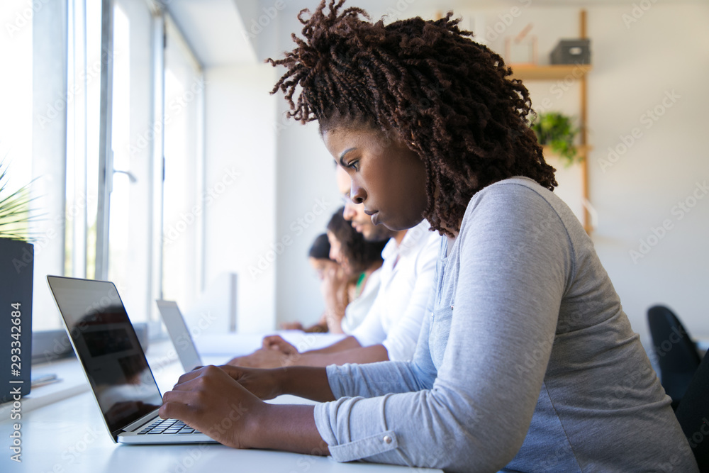 Focused African American worker using laptop in office. Line of man and ...