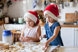 Fototapeta  - Children are cooking Christmas cookies in cozy home kitchen. Cute kids prepare holiday food for family. Funny little sisters in flour make pastries. Lifestyle candid moment. Children chef concept