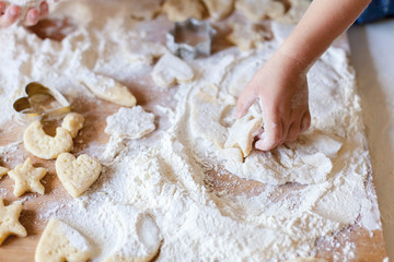 Child hands are cooking Christmas gingerbread cookies in home kitchen. Kid is playing with dough and flour. Little girl bake holiday homemade pastries. Children chef concept.