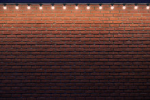 An Orange Brick Wall With Small Light Bulbs. Gradient Stone Background With Low Light And Copy Space. Place For Advert.