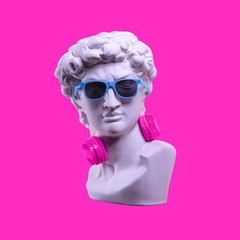 Wall Mural - Statue. Earphone on a pink background. Gypsum statue of David's head. Creative. Plaster statue of David's head in blue sunglasses. Minimal concept art.