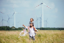 Mature Father With Small Daughter Walking On Field On Wind Farm.