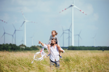 mature father with small daughter walking on field on wind farm.