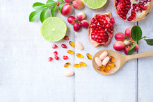 Vitamin Supplements On Wooden Spoon With Healthy Fruits Berry, Lime, Pomegranete On White Wooden Background.Top View.