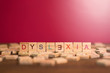 © Hafiez Razali - wooden alphabet blocks with DYSLEXIA word in the center on wooden table against pink background. Concept of Dyslexia awareness and human brain development