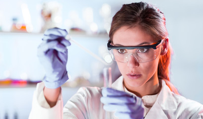 Poster - Life scientists researching in laboratory. Focused female life science professional pipetting solution into the glass cuvette. Lens focus on researcher's eyes. Healthcare and biotechnology concept.