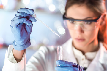 Poster - Life scientists researching in laboratory. Focused female life science professional pipetting solution into the glass cuvette. Lens focus on pipette. Healthcare and biotechnology concept.