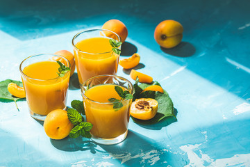 Wall Mural - Glass of fresh healthy apricot juice in sunny light on blue surface