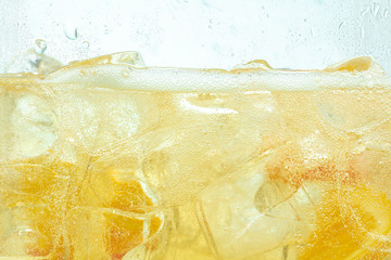 Close up of lemon slices in stirring the lemonade and ice cubes on background. Texture of cooling sweet summer's drink with macro bubbles on the glass wall. Fizzing or floating up to top of surface.