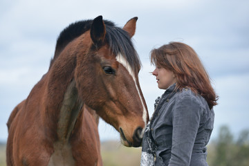 Wall Mural - Close up shot of pretty young woman sharing a loving moment with her large cob type bay horse.