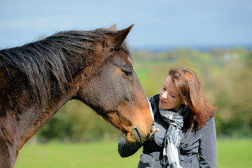 Wall Mural - clsoe up shot of pretty young woman and her beautiful bay horse sharing a loving moment in the field.