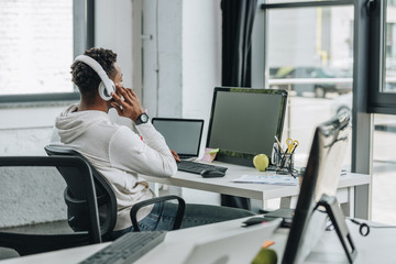 selective focus of african american programmer sitting at workplace in headphones