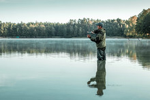 A Male Fisherman On The Lake Is Standing In The Water And Fishing For A Fishing Rod. Fishing Hobby Vacation Concept. Copy Space.