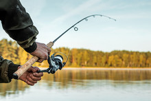 Hands Of A Man In A Urp Plan Hold A Fishing Rod, A Fisherman Catches Fish At Dawn. Fishing Hobby Vacation Concept. Copy Space.