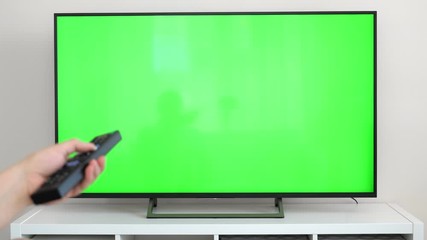 Watching tv with green screen at home interior. Push buttons on remote. Changing channels on television