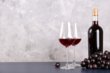 vintage bottle of red wine without label, two glasses and bunch of grapes on wooden table, grunged c