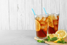 Glasses Of Refreshing Iced Tea On Light Table Against White Wooden Background. Space For Text