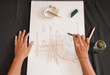 © Kemedo - First person view of a woman drawing with a pencil while smoking a marijuana joint. Black table with sketch, casual shell ashtray and cannabis.