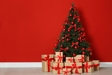 Decorated Christmas Tree And Gift Boxes Near Red Wall. Space For Text