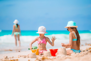 Mother and little daughters making sand castle at tropical beach