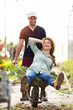 © Westend61 - Playful man and woman having fun with a wheelbarrow in a greenhouse