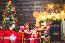 Wish You Merry Christmas. Surprised Woman. Beautiful Girl With Blond Hair And Red Lips Is Holding A Gift Box. Young Girl With Retro Hairstyle And Pinup Makeup Over Christmas Tree.