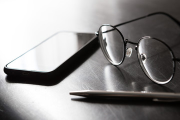 Wall Mural - Selective focus of Pen, glasses,  smartphone on black background and  copy space with light and shadow