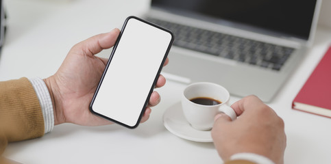 Businessman holding blank screen smartphone while drinking a cup of coffee