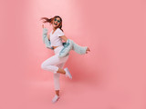 Inspired positive girl in white sneakers dancing on pink background. Gorgeous young female model with dark wavy hair jumping in studio. Not isolated. Copy space.