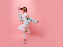  Inspired Positive Girl In White Sneakers Dancing On Pink Background. Gorgeous Young Female Model With Dark Wavy Hair Jumping In Studio. Not Isolated. Copy Space.