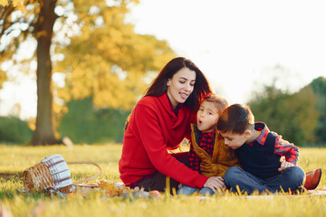 Wall Mural - Cute family in a autumn park. Happy mother with little kids. Family sitting on yellow leaves. Golden autumn.