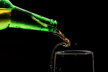 Close-up Of The Neck Of A Green Bottle With Drops Of Water And Pouring Cold Beer Into A Glass With Splash On A Black Background