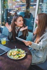 two young adult women have meeting in outdoors cafe working on laptop