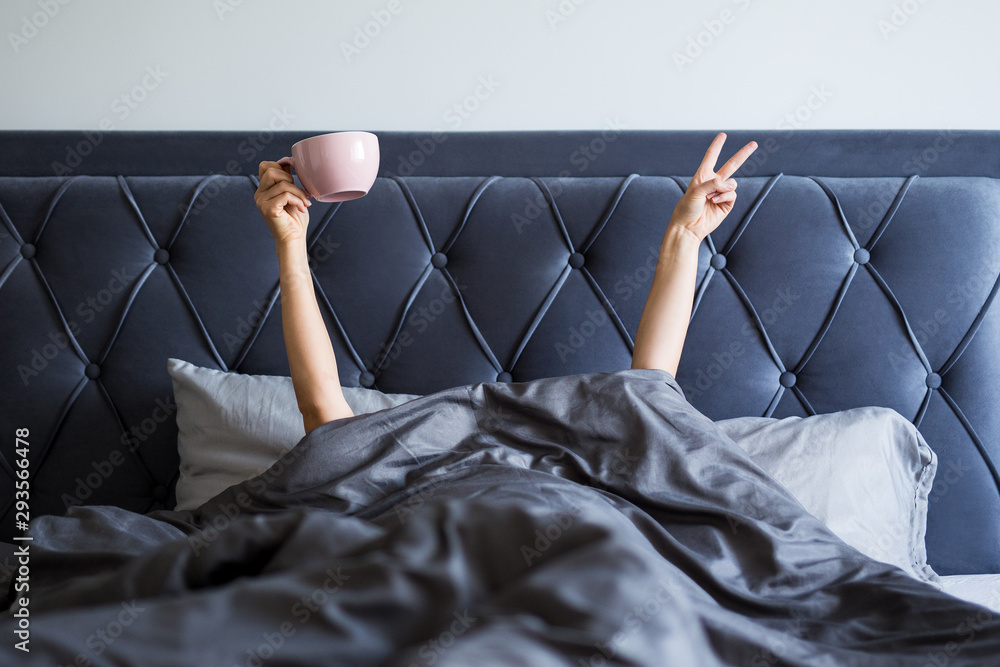 good morning concept - female hands with coffee mug and victory sign sticking out from the blanket - obrazy, fototapety, plakaty 