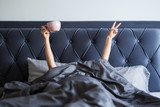 Fototapeta  - good morning concept - female hands with coffee mug and victory sign sticking out from the blanket