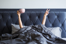 Good Morning Concept - Female Hands With Coffee Mug And Victory Sign Sticking Out From The Blanket