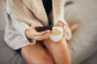 © chika_milan - Top view of caucasian woman using smart phone and holding cup of coffee while sitting on bed in morning.